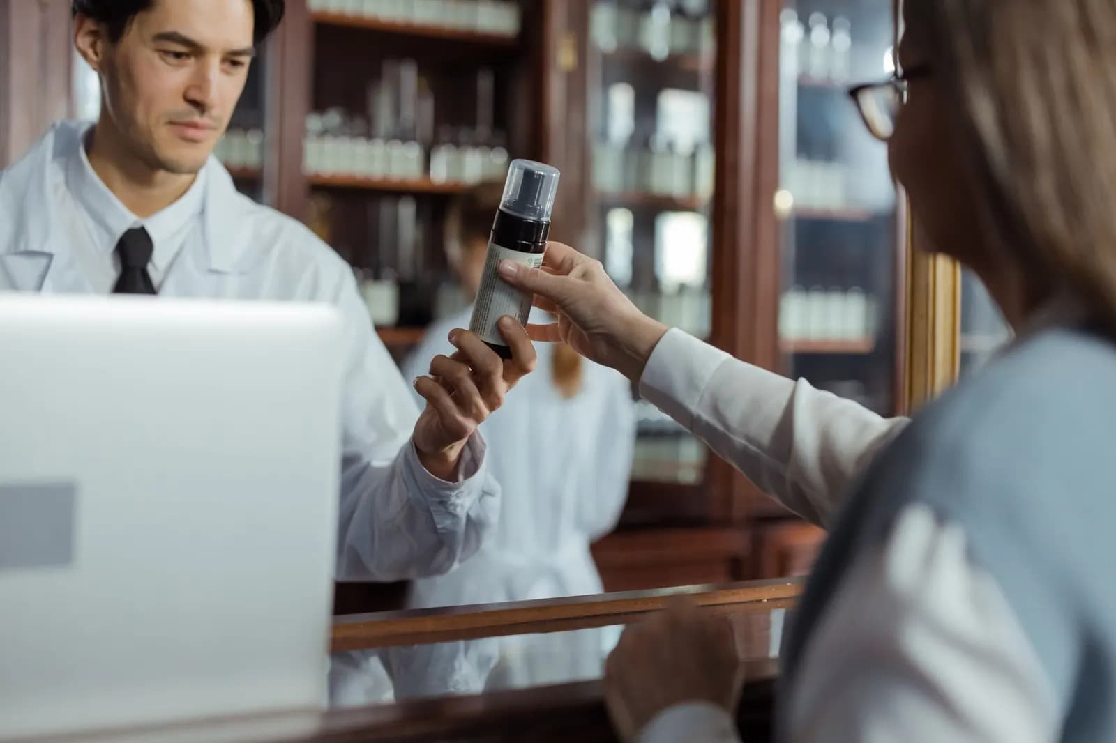 Φαρμακοποιός με λευκή μπλούζα δίνει προϊόν σε πελάτισσα στον πάγκο του φαρμακείου