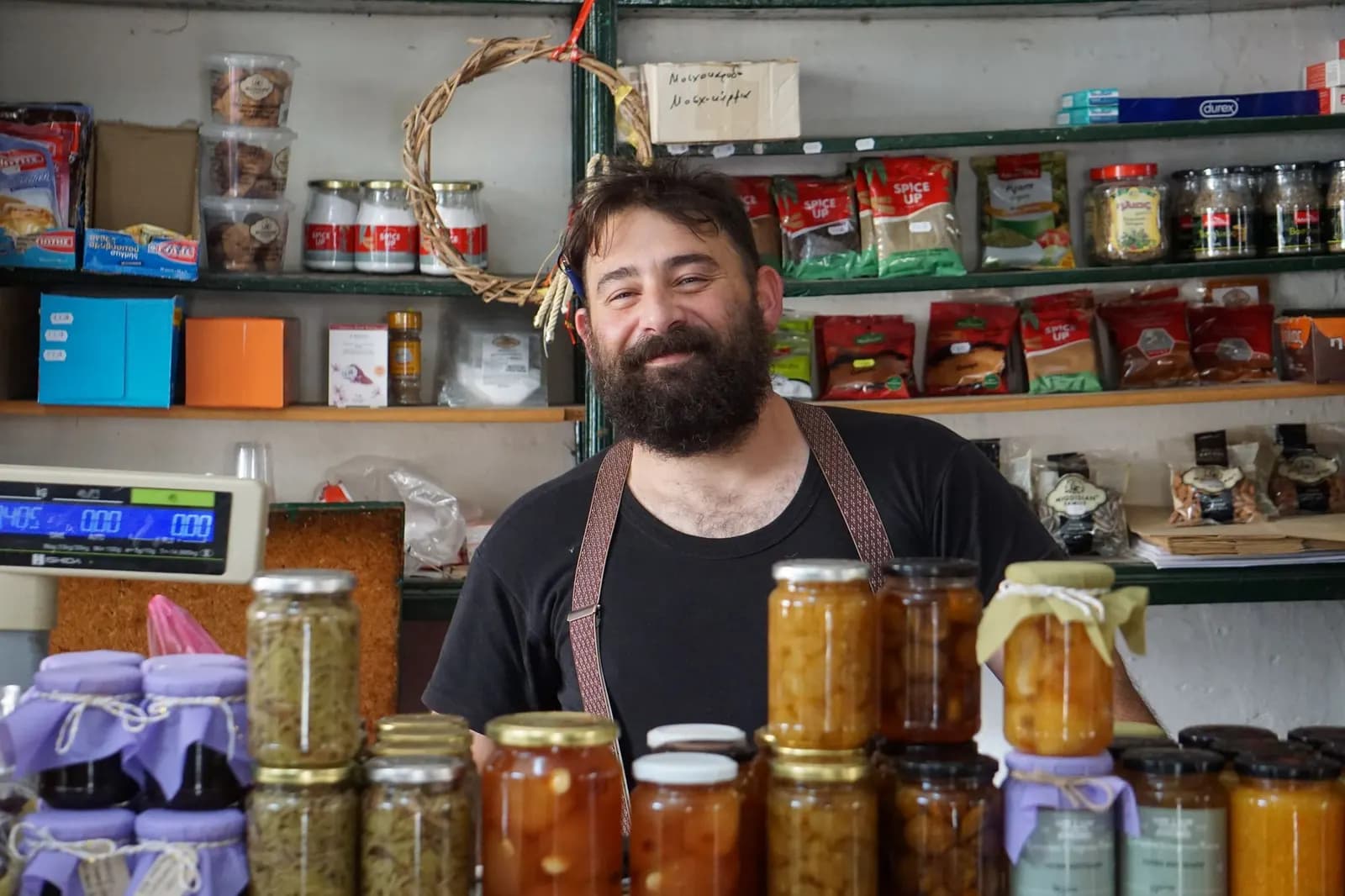 Χαμογελαστός ιδιοκτήτης μικρού καταστήματος πίσω από τον πάγκο με σπιτικές μαρμελάδες