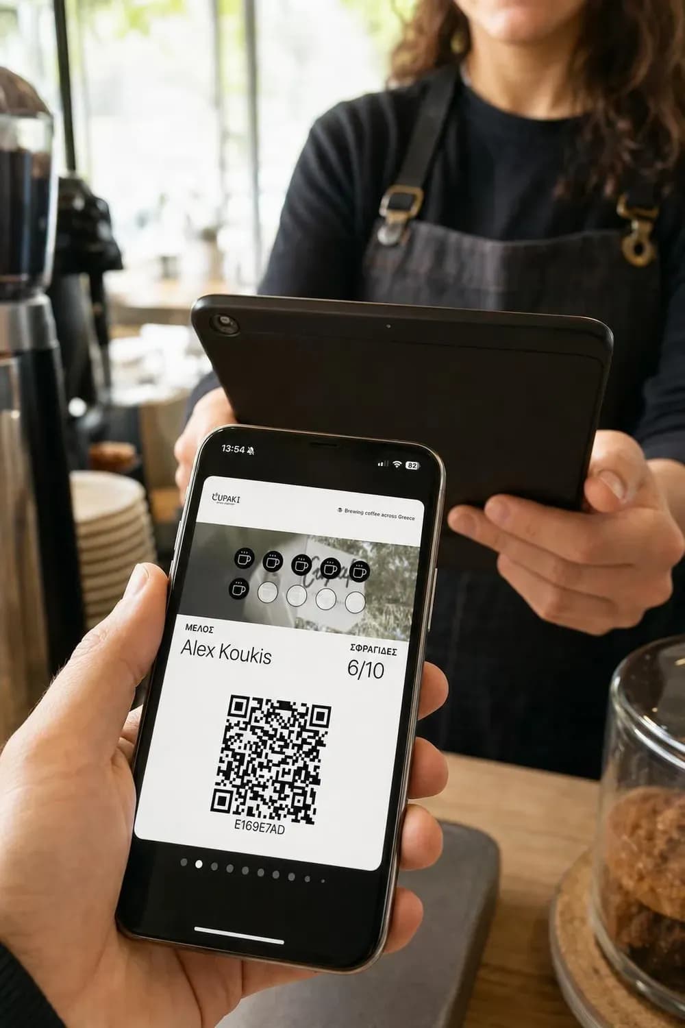 Barista σκανάρει με tablet το QR code της κάρτας CUPAKI στο iPhone του πελάτη για να προσθέσει σφραγίδα